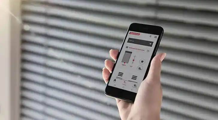 Smartphone Steuerung für Jalousien Person hält Smartphone mit Steuerungs-App vor Jalousien